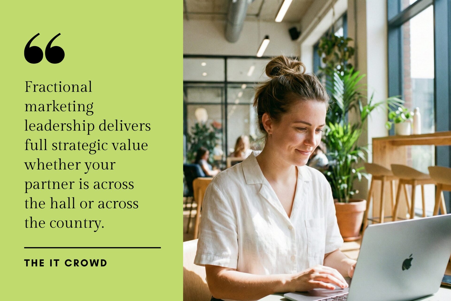 A smiling woman working on a MacBook laptop in a bright, plant-filled modern co-working cafe with people in the background.