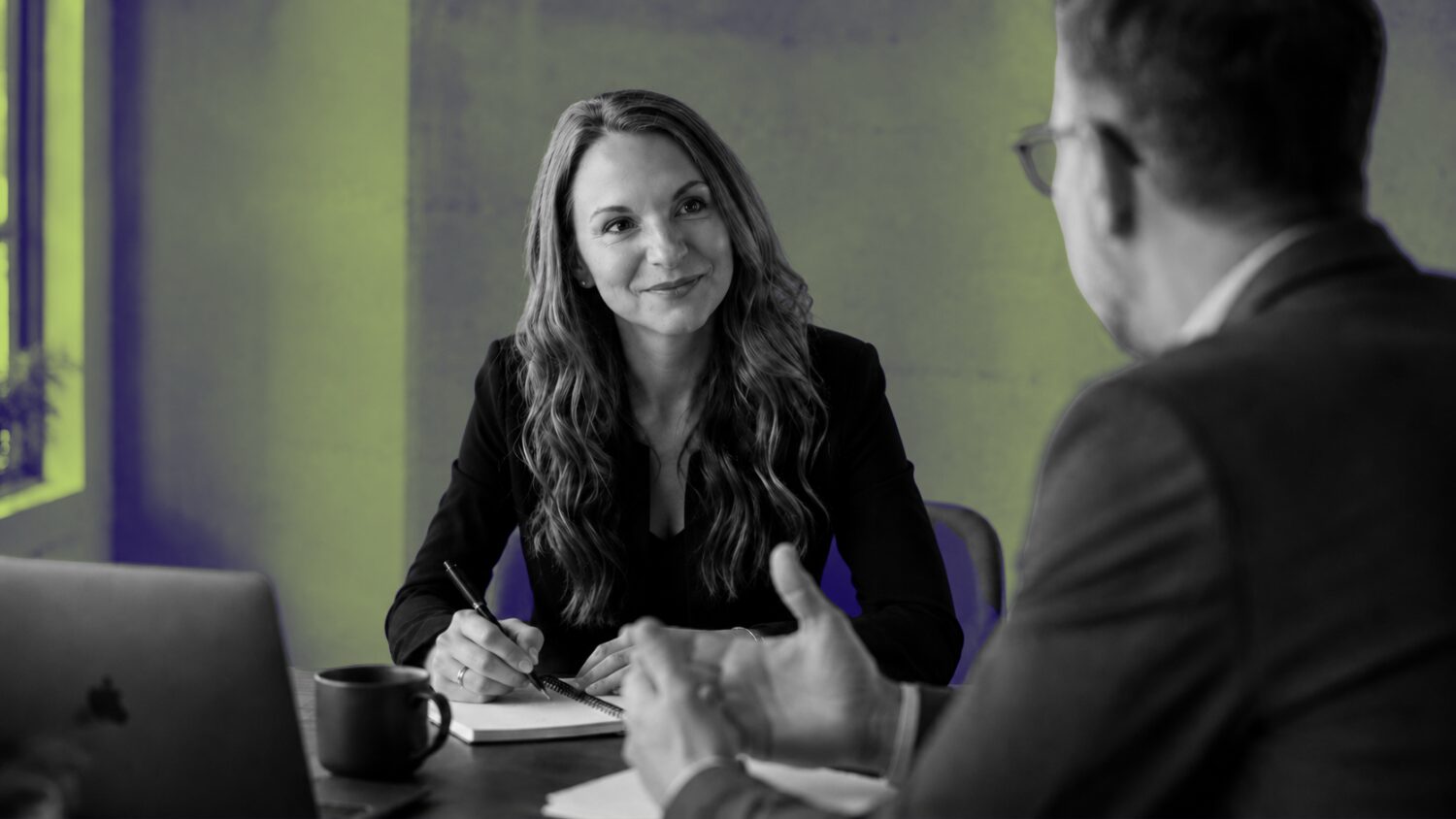 A marketing consultant in Dallas listens attentively and takes notes during a client strategy meeting.
