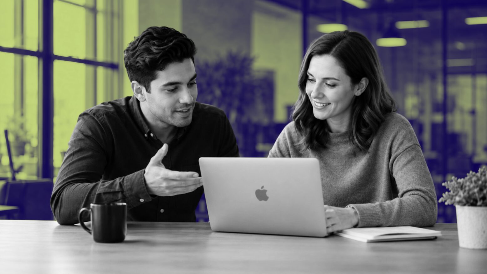 Two marketing professionals discuss content marketing services in Dallas over a laptop at a shared office desk with coffee.
